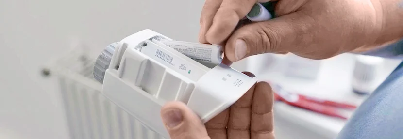 Person legt Batterien in Thermostat ein